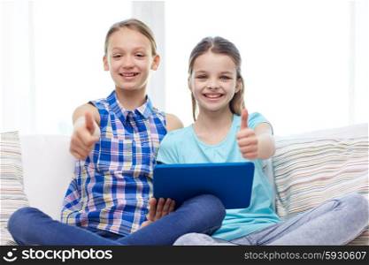 people, children, gesture, friends and friendship concept - happy little girls with tablet pc computer sitting on sofa and showing thumbs up at home