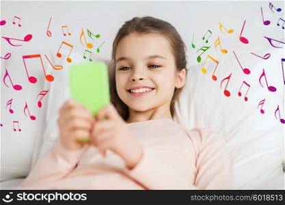 people, children, music and technology concept - happy smiling girl lying awake with smartphone in bed at home over musical notes