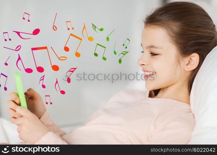 people, children, music and technology concept - happy smiling girl lying awake with smartphone in bed at home over musical notes