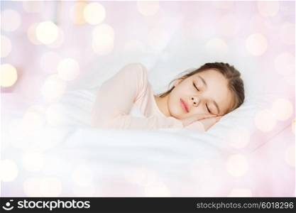 people, children, rest and comfort concept - girl sleeping in bed over lights