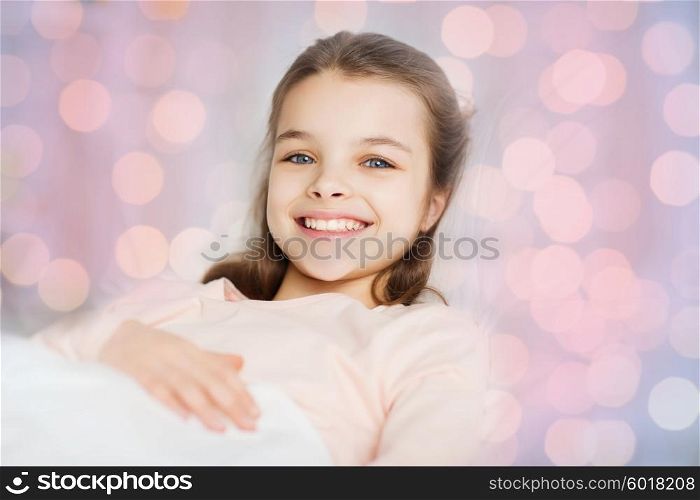 people, children, rest and comfort concept - happy smiling girl lying awake in bed over pink lights