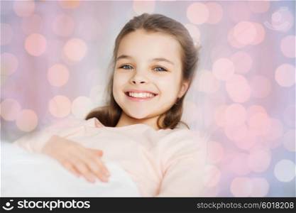 people, children, rest and comfort concept - happy smiling girl lying awake in bed over pink lights