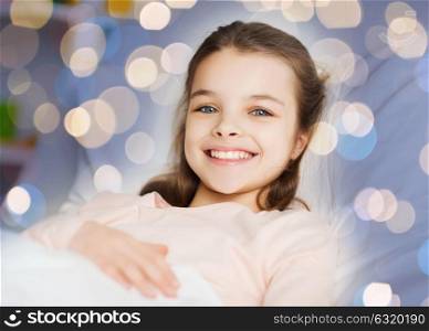people, children, rest and comfort concept - happy smiling girl lying awake in bed over holidays lights background. happy smiling girl lying awake in bed over lights