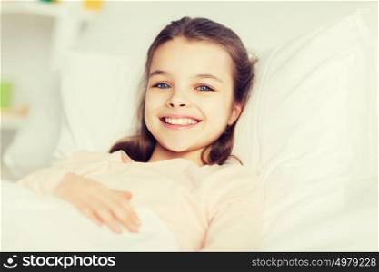 people, children, rest and comfort concept - happy smiling girl lying awake in bed at home. happy smiling girl lying awake in bed at home