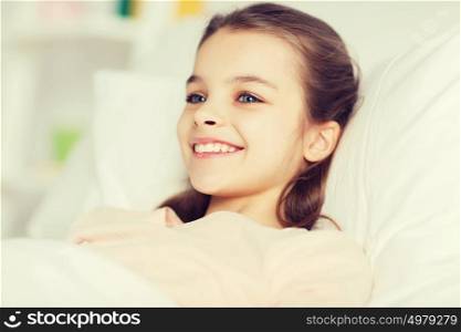 people, children, rest and comfort concept - happy smiling girl lying awake in bed at home. happy smiling girl lying awake in bed at home