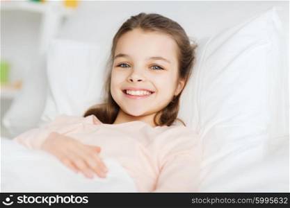 people, children, rest and comfort concept - happy smiling girl lying awake in bed at home