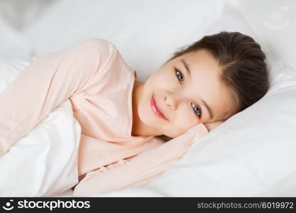 people, children, rest and comfort concept - happy smiling girl lying awake in bed at home
