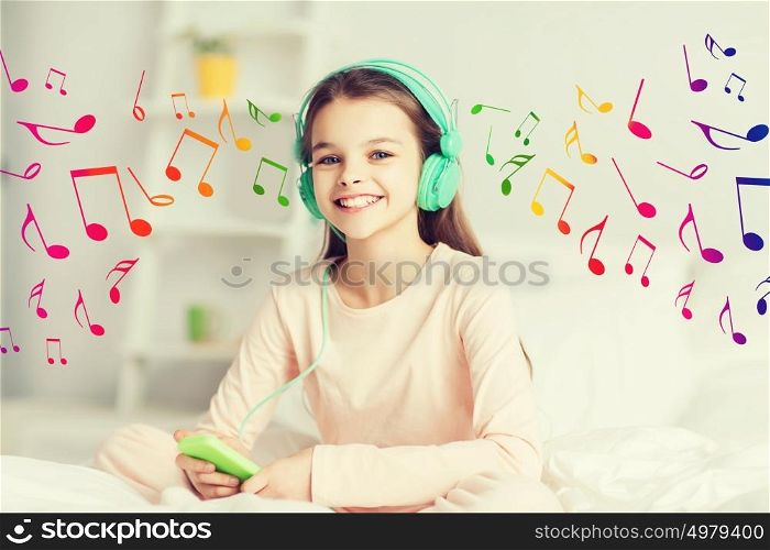 people, children, rest and technology concept - happy smiling girl lying awake with smartphone and headphones in bed listening to music at home. happy girl lying in bed with smartphone at home