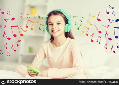 people, children, rest and technology concept - happy smiling girl lying awake with smartphone and headphones in bed listening to music at home. happy girl lying in bed with smartphone at home