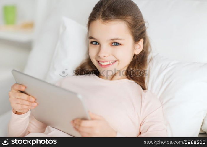 people, children, rest and technology concept - happy smiling girl lying awake with tablet pc computer in bed at home