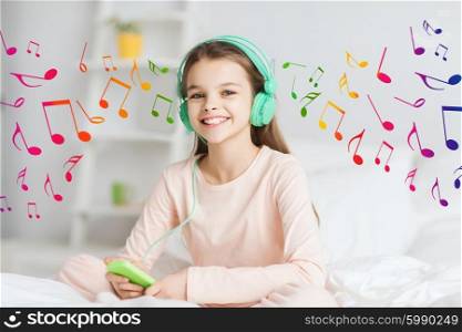 people, children, rest and technology concept - happy smiling girl lying awake with smartphone and headphones in bed listening to music at home