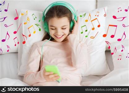 people, children, rest and technology concept - happy smiling girl lying awake with smartphone and headphones in bed listening to music at home