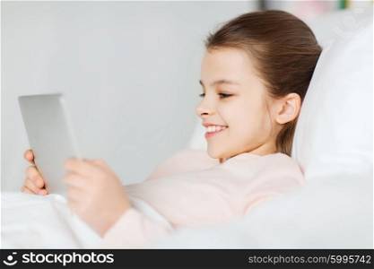 people, children, rest and technology concept - happy smiling girl lying awake with tablet pc computer in bed at home