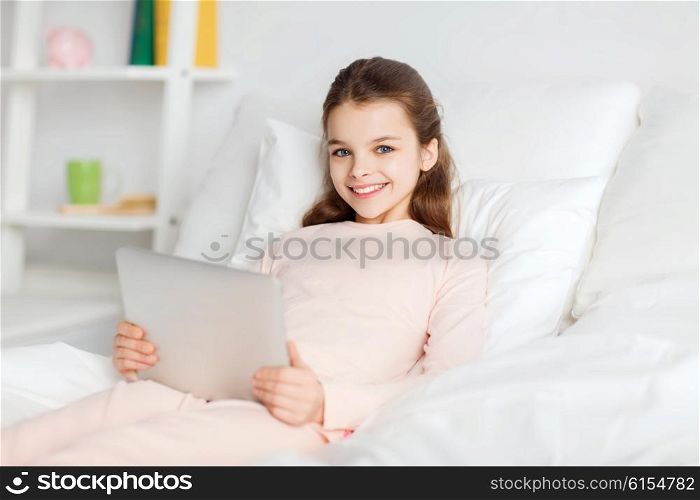 people, children, rest and technology concept - happy smiling girl lying awake with tablet pc computer in bed at home
