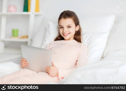 people, children, rest and technology concept - happy smiling girl lying awake with tablet pc computer in bed at home