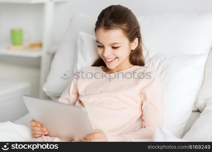 people, children, rest and technology concept - happy smiling girl lying awake with tablet pc computer in bed at home