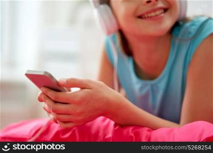 people, children, technology and leisure concept - close up of happy girl with headphones lying on bed and listening to music at home. girl in headphones listening to music at home