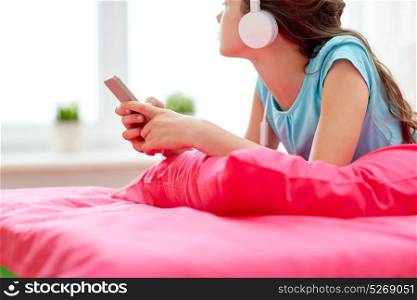 people, children, technology and leisure concept - girl with headphones lying on bed and listening to music at home. girl in headphones listening to music at home
