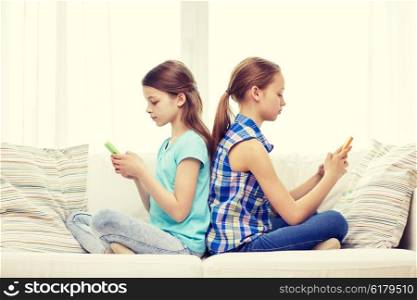 people, children, technology, friends and addiction concept - little girls with smartphones sitting on sofa back to back at home