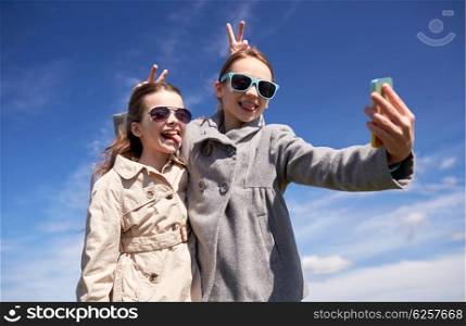 people, children, technology, friends and friendship concept - happy girls with smartphone taking selfie and making funny faces outdoors