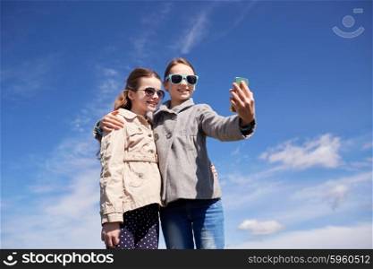 people, children, technology, friends and friendship concept - happy girls with smartphone taking selfie outdoors