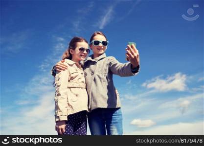 people, children, technology, friends and friendship concept - happy girls with smartphone taking selfie outdoors