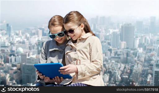 people, children, technology, friends and friendship concept - happy little girls in sunglasses with tablet pc computer over city background