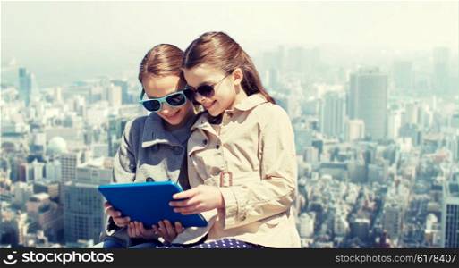 people, children, technology, friends and friendship concept - happy little girls in sunglasses with tablet pc computer over city background