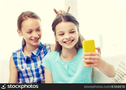 people, children, technology, friends and friendship concept - happy little girls taking selfie with smartphone and having fun at home