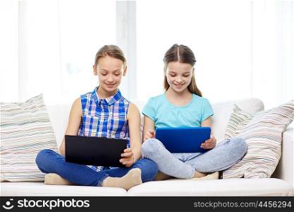 people, children, technology, friends and friendship concept - happy little girls with tablet pc computers sitting on sofa at home