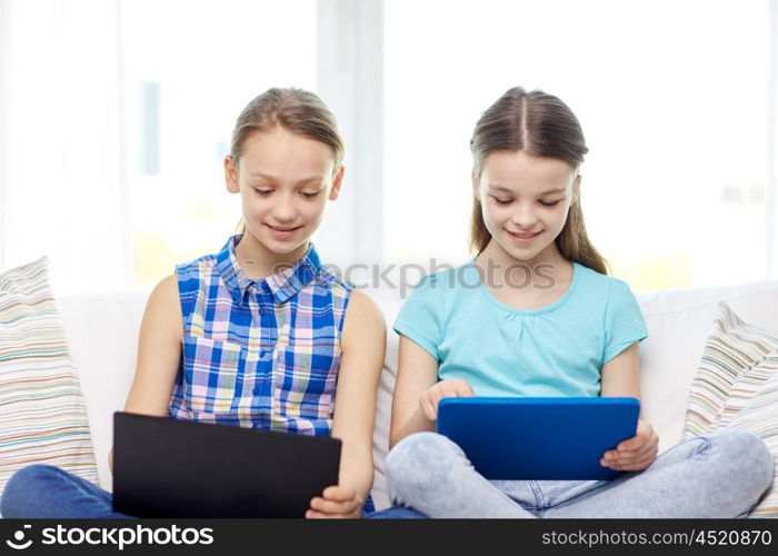 people, children, technology, friends and friendship concept - happy little girls with tablet pc computers sitting on sofa at home