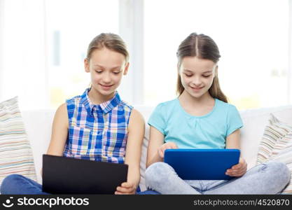 people, children, technology, friends and friendship concept - happy little girls with tablet pc computers sitting on sofa at home