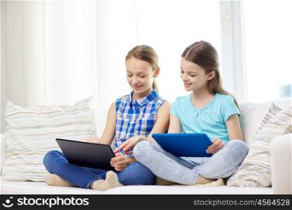 people, children, technology, friends and friendship concept - happy little girls with tablet pc computers sitting on sofa at home. happy girls with tablet pc sitting on sofa at home