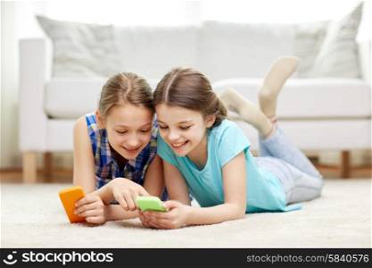 people, children, technology, friends and friendship concept - happy little girls with smartphones lying on floor at home