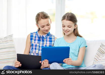 people, children, technology, friends and friendship concept - happy little girls with tablet pc computers sitting on sofa at home