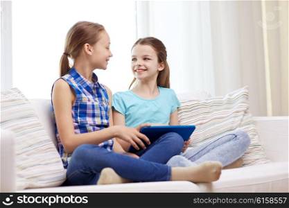 people, children, technology, friends and friendship concept - happy little girls with tablet pc computer sitting on sofa and talking at home