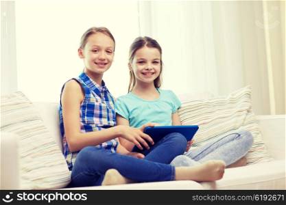 people, children, technology, friends and friendship concept - happy little girls with tablet pc computer sitting on sofa at home