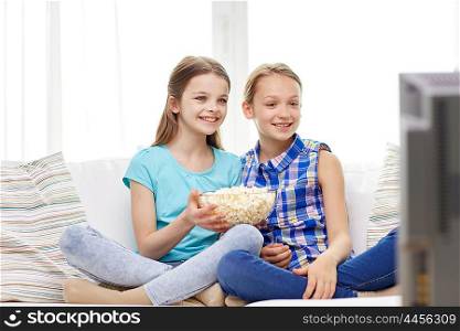 people, children, television, friends and friendship concept - two happy little girls with popcorn watching tv at home