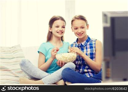 people, children, television, friends and friendship concept - two happy little girls watching comedy movie on tv and eating popcorn at home
