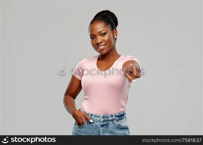people, choice and gesture concept - happy african american young woman pointing finger to you over pink background. african american woman pointing finger to you