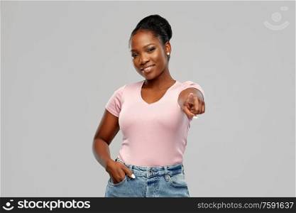 people, choice and gesture concept - happy african american young woman pointing finger to you over pink background. african american woman pointing finger to you