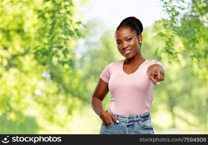 people, choice and gesture concept - happy african american young woman pointing finger to you over green natural background. african american woman pointing finger to you