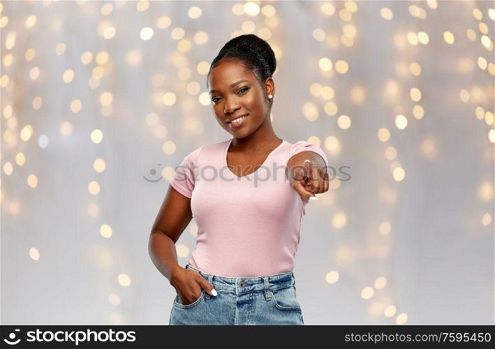 people, choice and holidays concept - happy african american young woman pointing finger to you over festive lights background. african american woman pointing finger to you