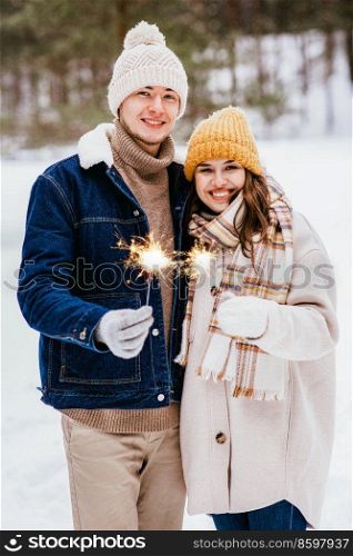 people, christmas and holidays concept - happy smiling couple with sparklers in winter forest. happy couple with sparklers in winter forest