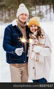 people, christmas and holidays concept - happy smiling couple with sparklers in winter forest. happy couple with sparklers in winter forest
