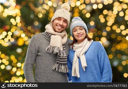 people, christmas and winter clothes concept - happy couple in knitted hats and scarves over festive lights background. happy couple in winter hats over christmas lights