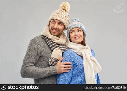 people, christmas and winter clothes concept - happy couple in knitted hats and scarves over grey background. happy couple in winter clothes