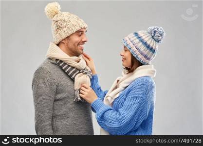 people, christmas and winter clothes concept - happy couple in knitted hats and scarves over grey background. happy couple in winter clothes