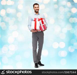 people, christmas, birthday and holidays concept - happy young man holding gift boxes over blue lights background