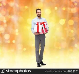 people, christmas, birthday and holidays concept - happy young man holding gift boxes over lights background